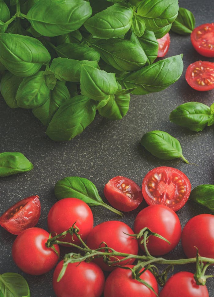 Home Organic basil leaves with ripe tomatoes on a rustic countertop, highlighting fresh ingredients for cooking.