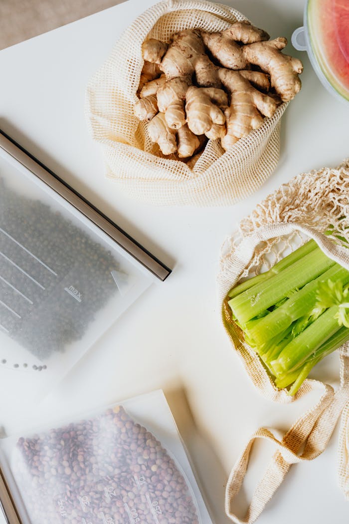 About Flat lay image showcasing fresh ginger roots, celery, and beans on a white surface.